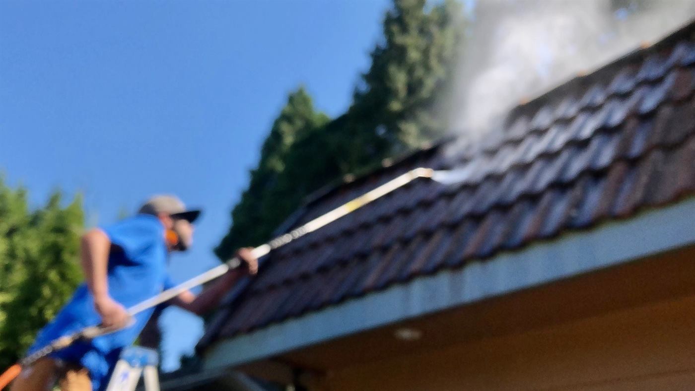 An Easy Flow Gutter Co. crew member in a branded shirt washing a roof from a ladder in Eugene, Oregon