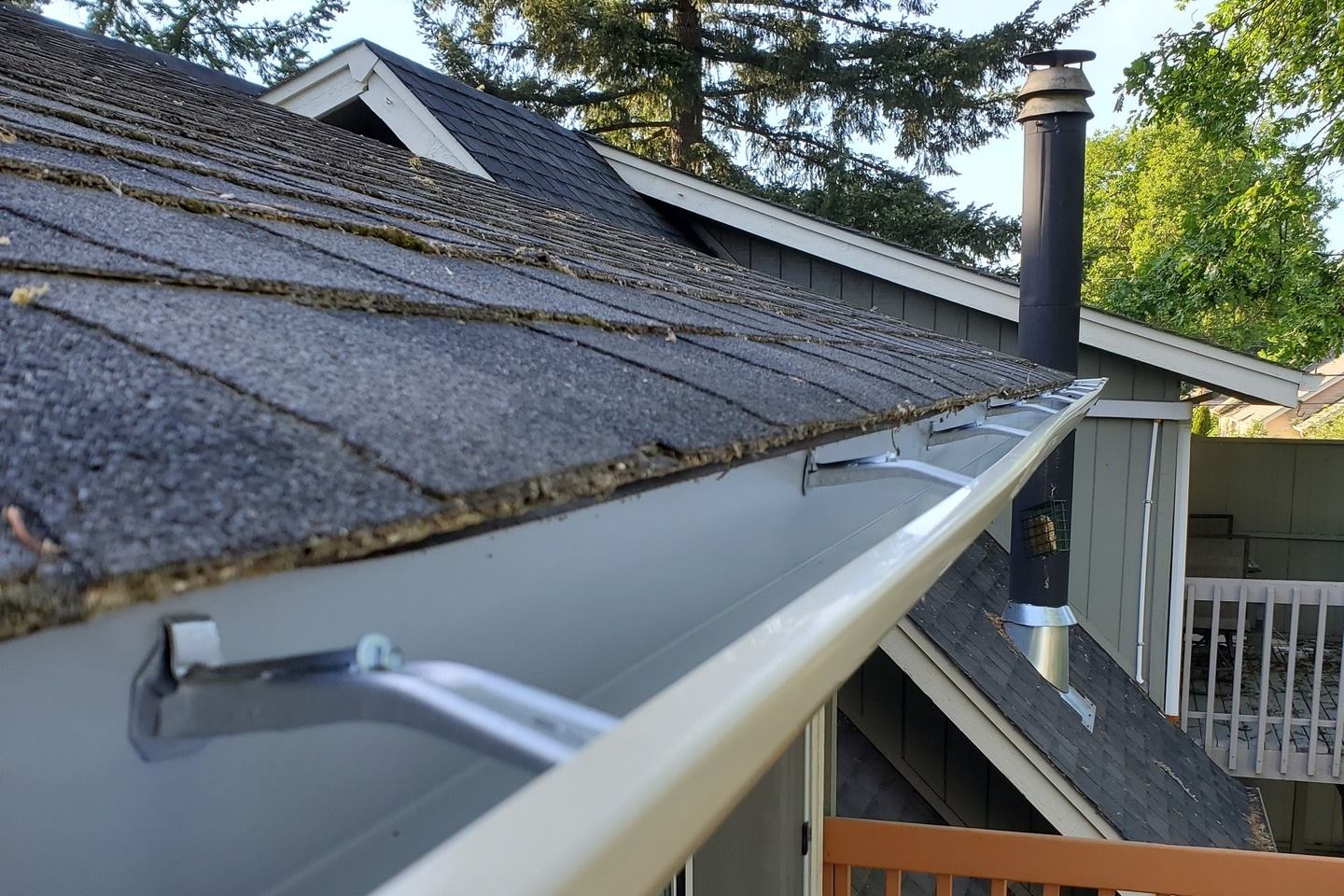 A newly installed seamless aluminum gutter with hidden hangers running along a shingle roof in Eugene, Oregon